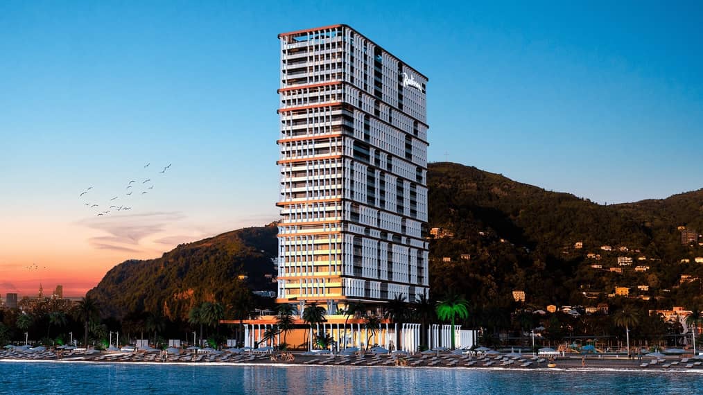 Реалистичная 3D-визуализация многоэтажного отеля Radisson Blu, расположенного на первой береговой линии с пляжем и горами на заднем плане.